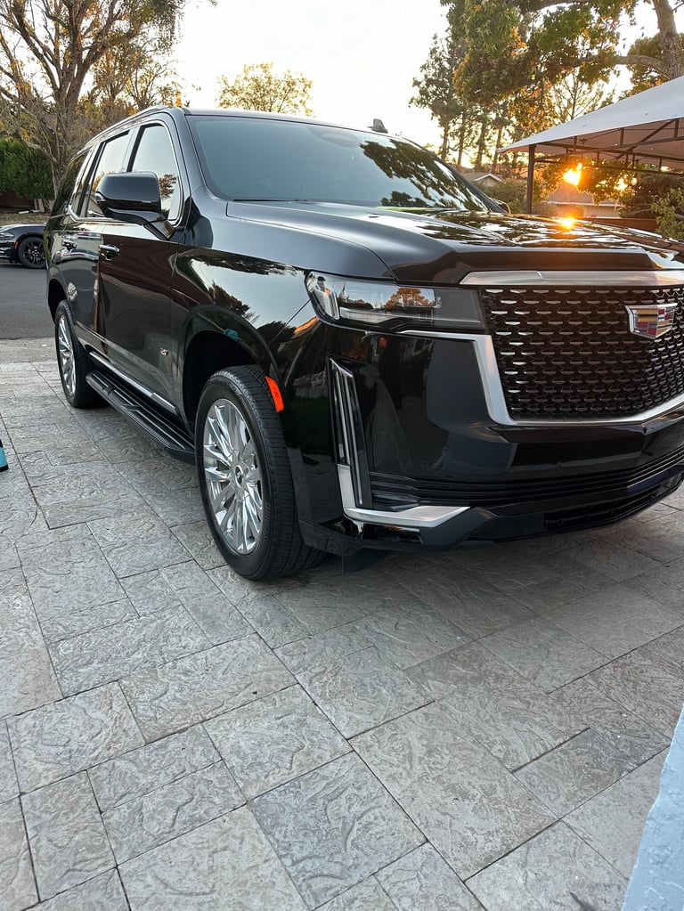Black luxury SUV parked in driveway with trees and sunset lighting in background