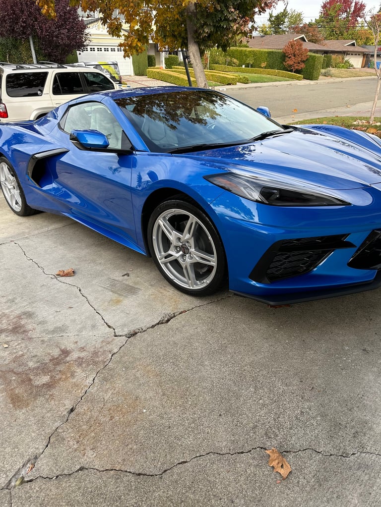 Blue Chevrolet Corvette sports car parked in residential driveway with open door