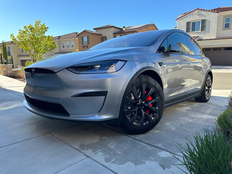 Silver Tesla Model X electric SUV parked in a residential driveway on a sunny day
