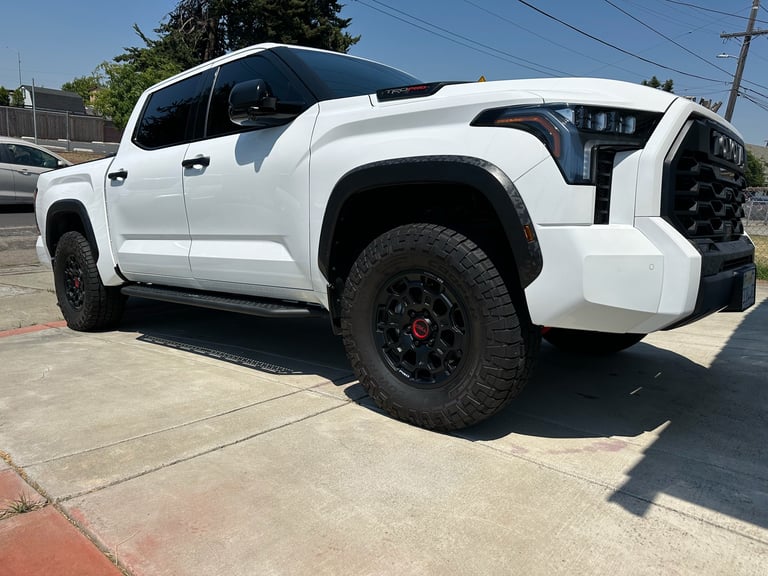 White Toyota Tundra pickup truck with black wheels parked on a paved lot in daylight