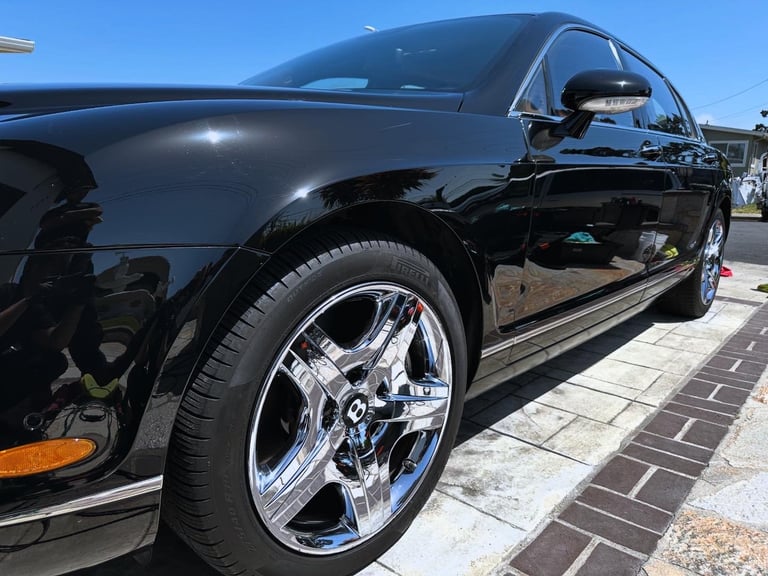 Black luxury car with chrome wheels parked on brick surface under clear blue sky