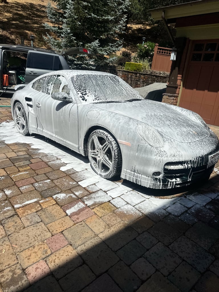 White sports car covered in soap suds parked in a driveway during car wash