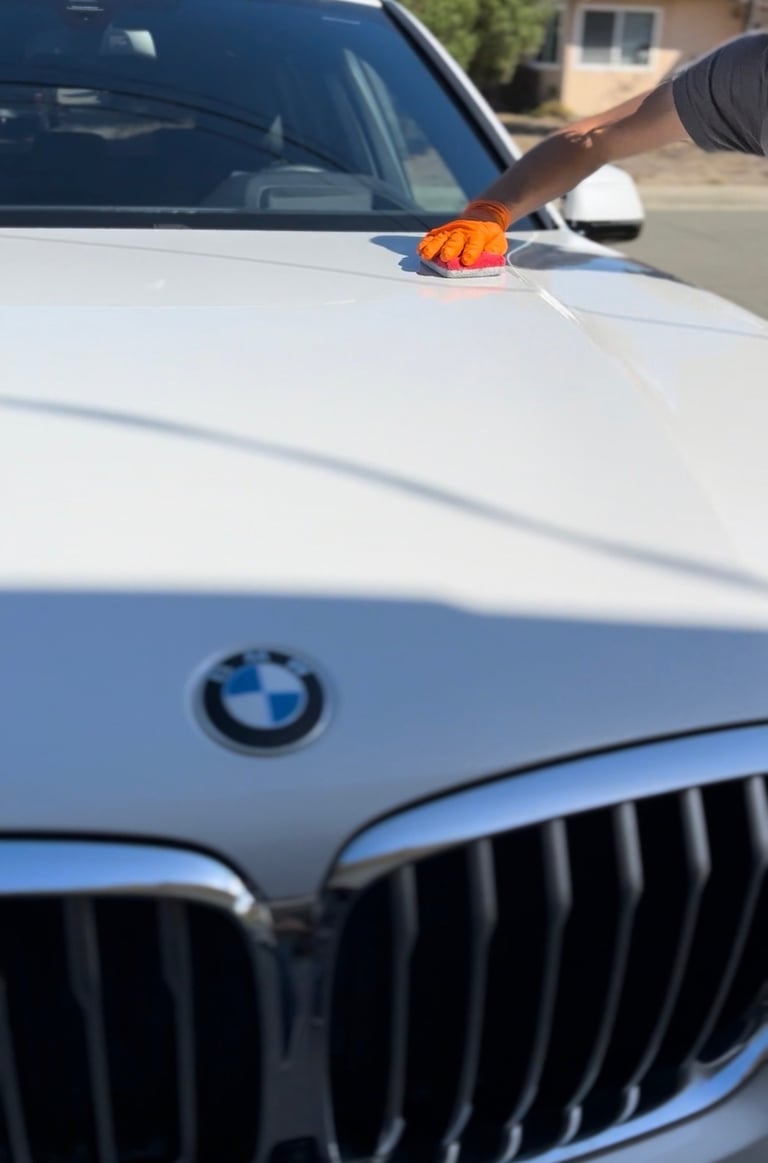 Person with microfiber cloth washing white BMW car hood on sunny day