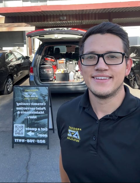 Young man wearing glasses and black polo shirt smiling at camera with open van displaying organizational products behind him